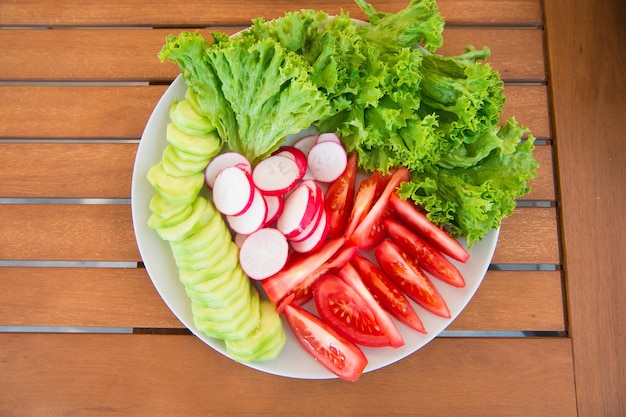 Geschmack von Frische. Frisches Gemüse auf Teller. Frühlingssalat. Gehackte Tomaten, Gurken-Rettich und Salat. Frischer Salat aus heimischem Bio-Gemüse. Vegetarisches Lebensmittelkonzept. Frisches Essen.