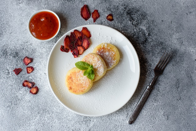 Geschmackvolle frische Hüttenkäsepfannkuchen auf einer weißen Platte auf einem konkreten Hintergrund. Gesundes und Diätfrühstück