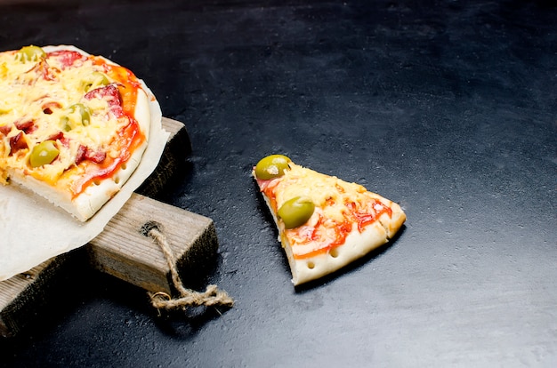 Geschmackvolle Pizza mit Gewürzen und Oliven auf einem schwarzen Hintergrund