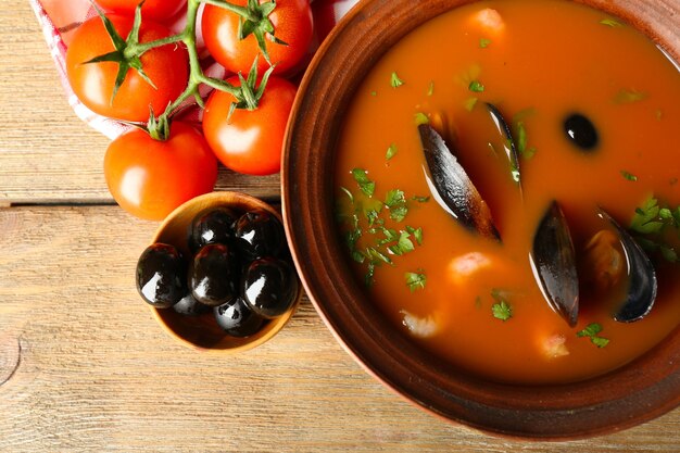 Foto geschmackvolle suppe mit garnelen, muscheln, tomaten und schwarzen oliven in einer schüssel auf holzgrund