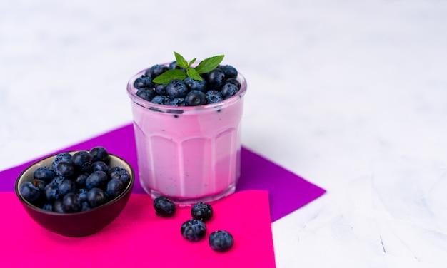 Geschmackvoller frischer Blaubeerjoghurt-Erschütterungsnachtisch im Glas, das auf purpurroter Serviette der weißen Tabelle steht. Selbst gemachter Beerensmoothie. Gesundes Essen. Diät Essen Joghurt