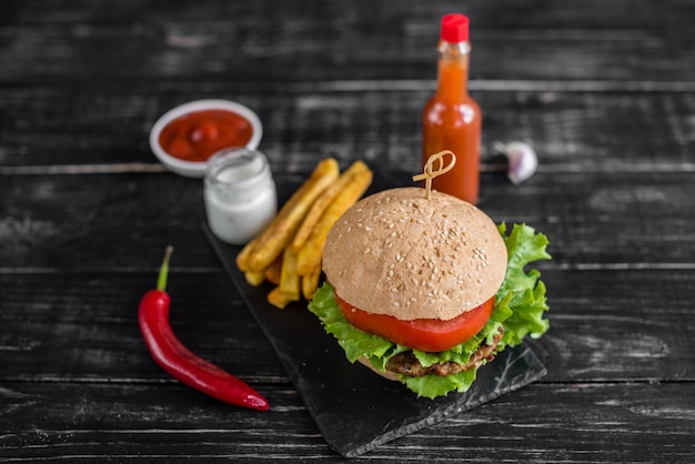 Geschmackvoller Hamburger mit Fleisch und Gemüse gegen einen dunklen Hintergrund. Fast Food. Es kann als Hintergrund verwendet werden