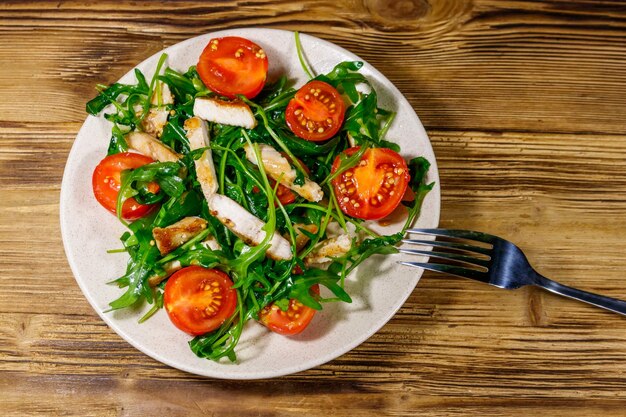 Foto geschmackvoller salat aus gebratener hühnerbrust, frischer rucola und kirschtomaten auf einem holztisch