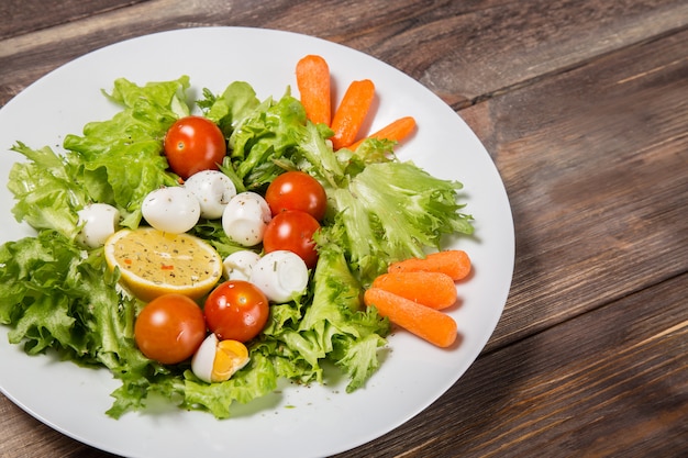 Geschmackvoller salat mit kirschtomaten, salatblättern, zitrone, gewürzen, karotte und wachteleiern auf holztisch