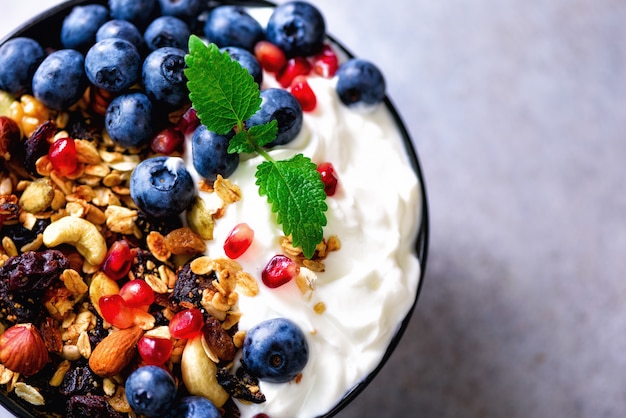 Geschmackvolles selbst gemachtes Granola, Joghurt, frische organische Beeren, Granatapfel, Minze auf grauem Beton