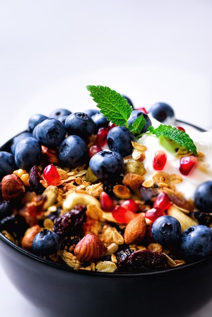 Geschmackvolles selbst gemachtes Granola, Joghurt, frische organische Beeren, Granatapfel, Minze auf grauem Beton