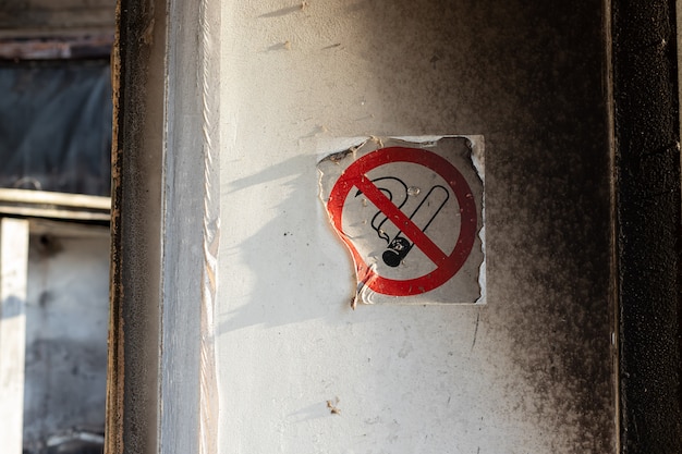 Geschmolzener Aufkleber mit einem Rauchverbotsschild an der Wand mit Spuren von schwarzem Ruß von einem Feuer