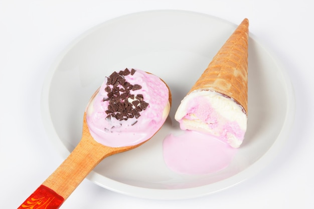 Geschmolzenes Eis mit Waffelkegel und Holzlöffel auf weißem Teller isoliert auf weißem Hintergrund Rosa Eis auf einem weißen Teller Nahaufnahme
