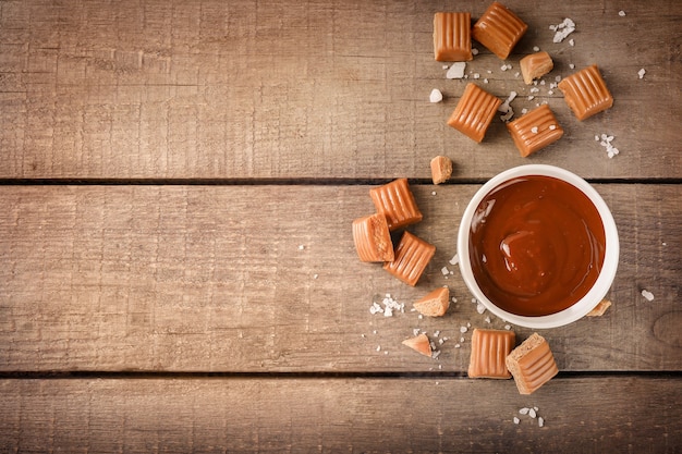 Geschmolzenes Karamell in einer Schüssel mit gesalzenen Karamellbonbons auf Holz