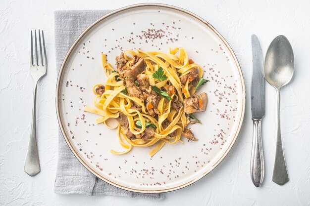 Geschmortes Kaninchen mit Rosmarin, Knoblauch und Pasta Tagliatelle oder Pappardelle-Set, auf Teller, auf weißem Stein