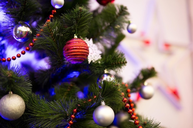 Geschmückte Weihnachtsbäume in Nahaufnahme. Rote und goldene Kugeln und beleuchtete Girlanden mit Taschenlampen.