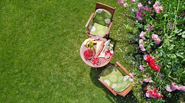 Geschmückter Tisch mit Broterdbeere und Früchten im schönen Sommerrosengarten-Luftbild von oben