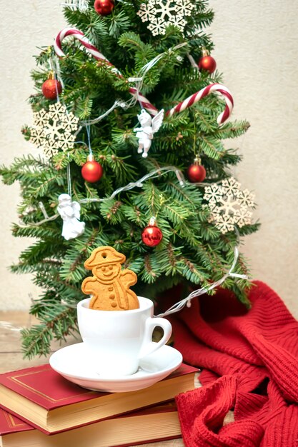 Geschmückter Weihnachtsbaum mit einer Tasse Tee, Kaffee und Ingwerplätzchen, Bällen, Schneeflocken, Zuckerstangen, Engeln, Lichtergirlande, festlichem Dekor. Weihnachten, Neujahr Dekorationen. Winterurlaub Konzept.