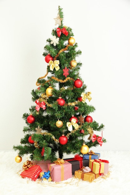 Geschmückter Weihnachtsbaum mit Geschenken auf grauem Wandhintergrund