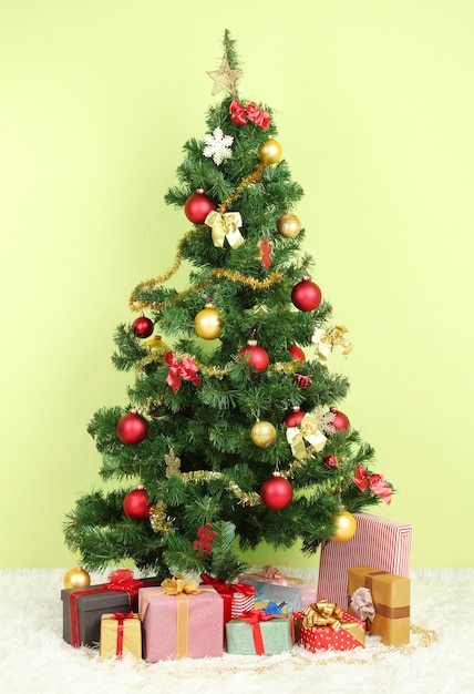 Geschmückter Weihnachtsbaum mit Geschenken auf grünem Wandhintergrund