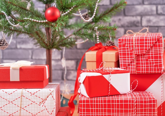 Geschmückter Weihnachtsbaum mit verpackten schönen rot-weißen Geschenken zu Hause mit schwarzer Backsteinmauer, festliches Designkonzept, Nahaufnahme.