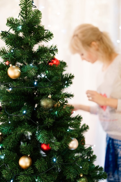 geschmückter Weihnachtsbaum und ein verschwommenes Mädchen, das es anzieht.