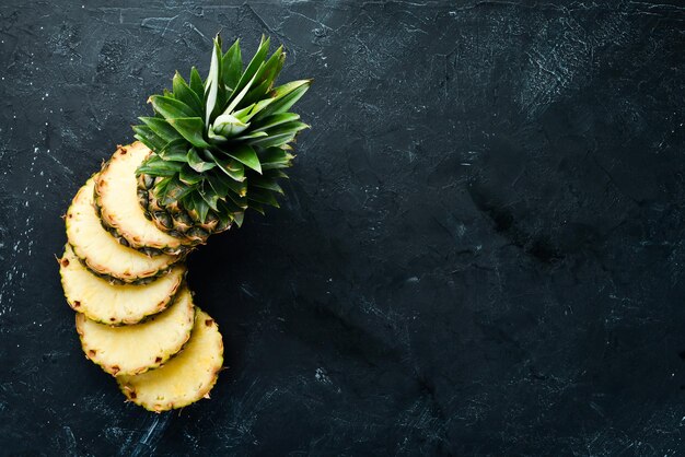 Geschnittene Ananas auf schwarzem Hintergrund. Tropische Früchte. Ansicht von oben. Freier Kopienraum.