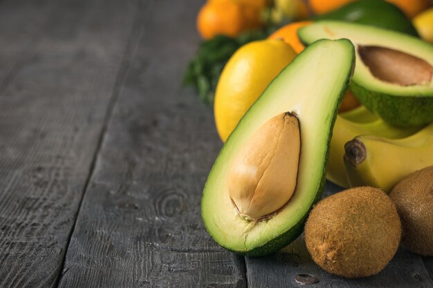 Geschnittene Avocado, Tangerinen, Orangen, Kiwi und Bananen auf schwarzer Tabelle der Weinlese. Vegetarisches Essen.