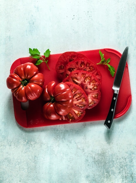 Geschnittene Beefsteak-Tomate auf einem roten Schneidebrett und einem Messer. gesunde Sommergerichte kochen