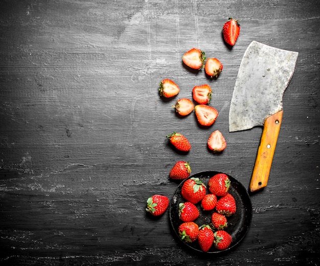 Geschnittene Erdbeeren mit dem alten Beil. Auf dem schwarzen Holztisch.