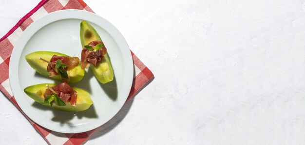 Geschnittene frische Melone mit Schinken mit Sonnenlicht auf bunten Hintergründen. Spanisches Essenskonzept