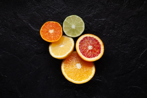 Geschnittene frische reife Zitrusfrüchte. Zitrone, rote Orange, Limette und Mandarine auf schwarzem Steinhintergrund.