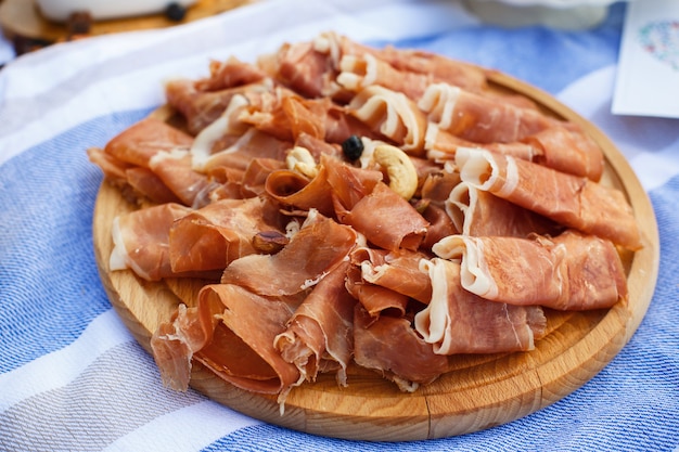 Geschnittene frische Rollen von Jamon auf hölzernem Behälter an der Picknickdecke. Sommerwochenenden