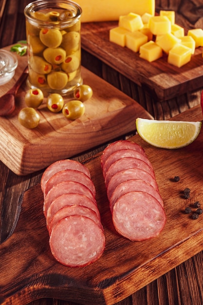 Geschnittene geräucherte Salami auf Schneidebrett mit Jungen von Käse und Oliven