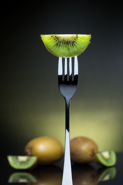 Geschnittene grüne Kiwi auf der Gabel mit ganzer Kiwi im Hintergrund