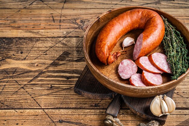 Geschnittene kalte geräucherte Wurst in einer Holzplatte mit Thymian. hölzerner Hintergrund. Ansicht von oben. Platz kopieren.