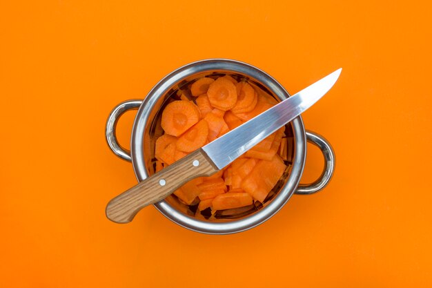 Geschnittene Karotten in einer Metallkasserolle mit einem Messer auf einem orange Hintergrund