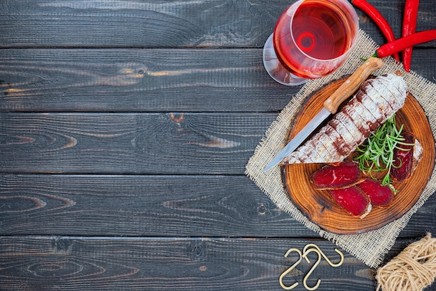 Geschnittene kurierte Bresaola mit Gewürzen und einem Glas Rotwein auf dunklem rustikalem Holzhintergrund.