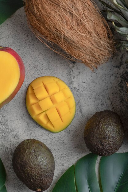 Geschnittene Mango-, Kokos- und reife Avocado-Früchte auf Marmoroberfläche.