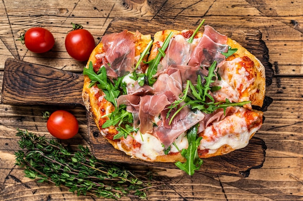 Geschnittene Pizza mit Prosciutto Parmaschinken, Rucola und Parmesankäse auf einem Holzbrett. hölzerner Hintergrund. Ansicht von oben.