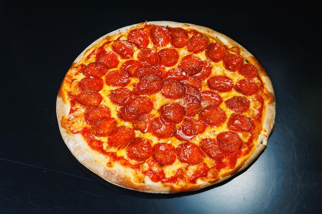 Geschnittene Pizza mit Wurst, Tomatensauce, Mozzarella-Zwiebeln und Teigrand mit Frischkäse auf schwarzem Hintergrund