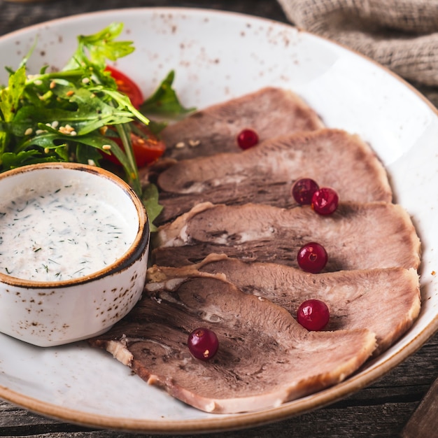 Geschnittene Rinderzunge mit Preiselbeeren, Salat und Sauce