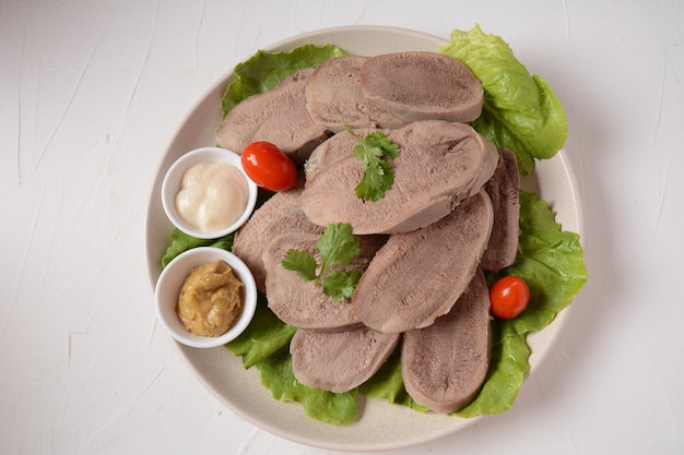 Geschnittene Rinderzungenscheiben auf einer Platte mit Salatblättern, Kirschtomaten und Dijon-Senf auf Holzuntergrund