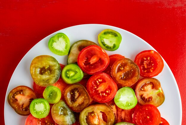 Geschnittene rote, grüne und kumato Tomaten auf weißer Platte auf rotem hölzernem Hintergrund