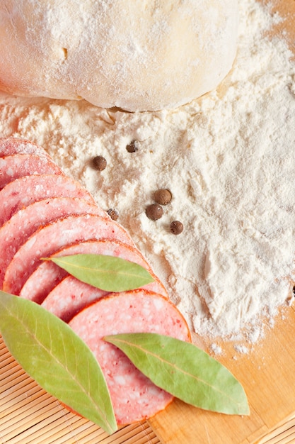 Geschnittene Salami, Lorbeerblätter und Teig