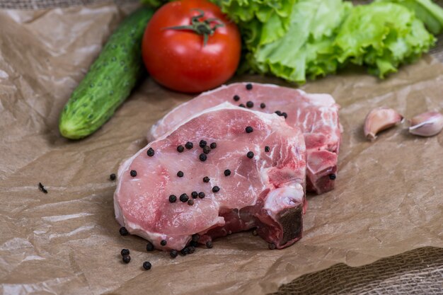 Geschnittene Stücke rohes Fleisch zum Grillen mit frischen Gemüsetomaten, Salat auf Holzoberfläche.