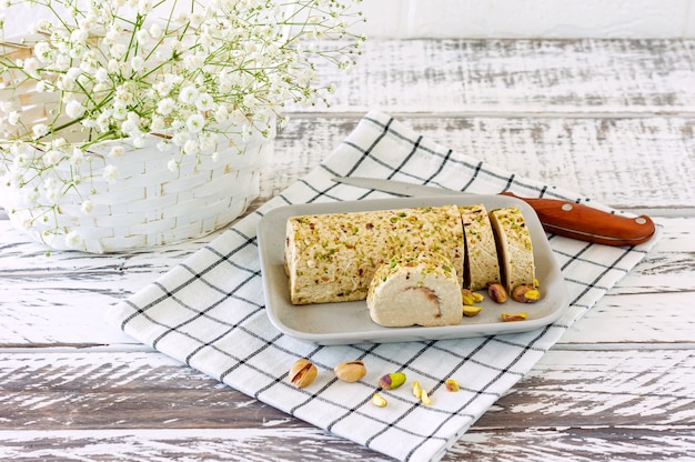 Geschnittene Tahini-Halva mit Pistazie auf einem weißen Holzschreibtisch, der mit Blumen verziert ist.