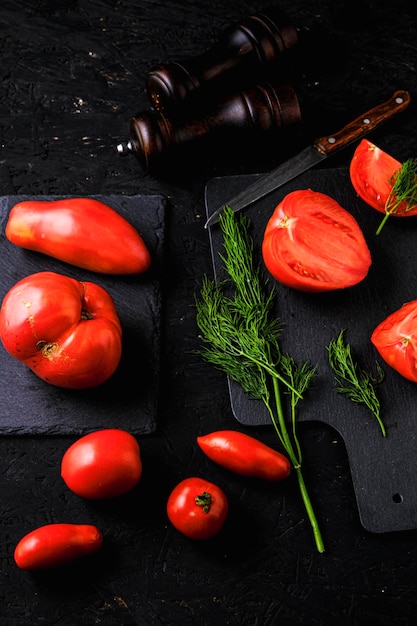 Geschnittene Tomaten auf einem Schiefer Dill grünt zwei Gewürzmühlen und Messer mit Holzgriff auf dunklem Hintergrund