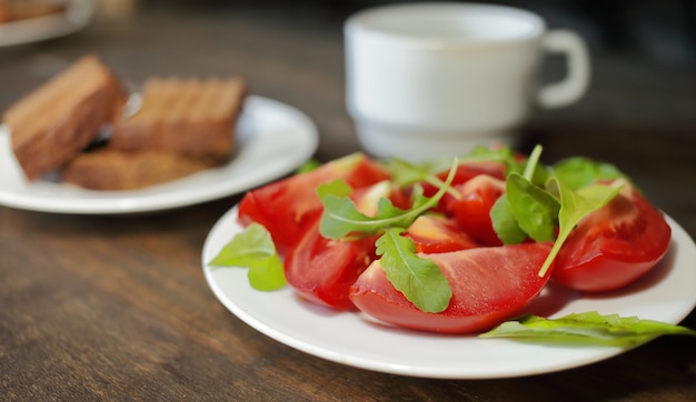 Geschnittene Tomaten mit Salat auf einem weißen Teller und Brot