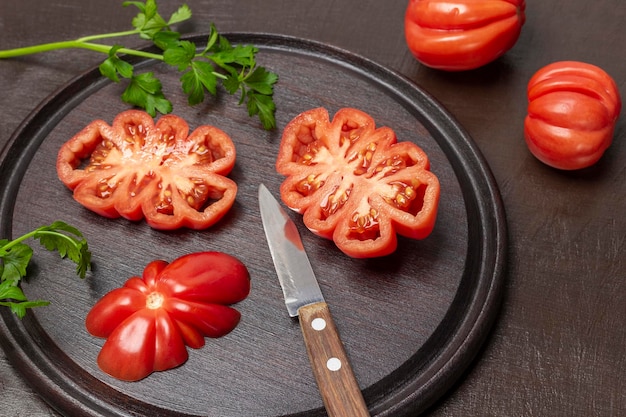 Geschnittene Tomaten und Messer auf Schneidebrett Zwei ganze Tomaten auf dem Tisch