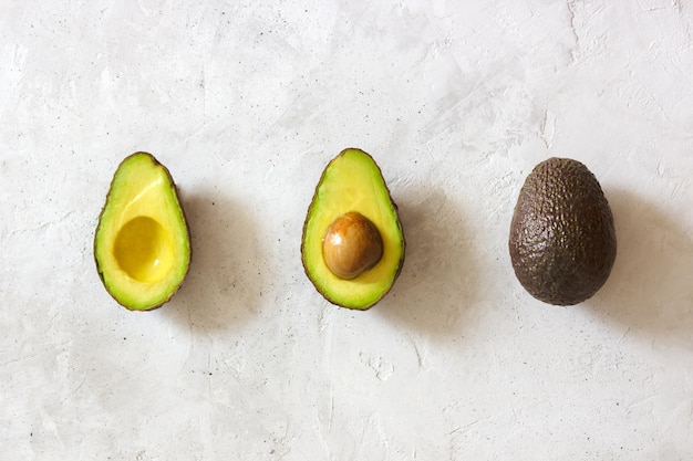 Geschnittene und ganze Avocado, die auf einer Linie auf der grauen Tischplatte liegen