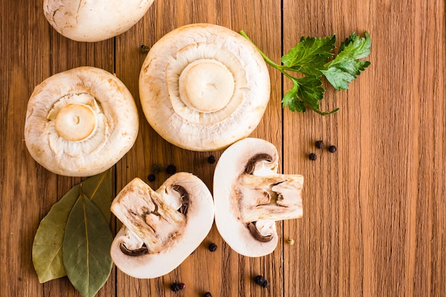 Geschnittene und ganze Champignons, Lorbeerblatt, Petersilie und schwarzer Pfeffer auf einem Holztisch. Ansicht von oben