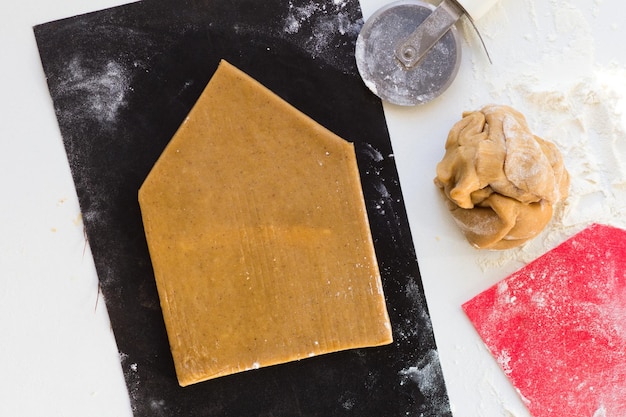 Geschnittene Wand des Lebkuchenhauses aus rohem Lebkuchenteig auf schwarzem Teflon-Backblech auf weißem Hintergrund