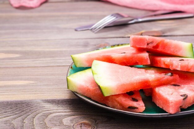 Geschnittene Wassermelone auf einer keramischen Platte, einem Tischbesteck und einer Serviette auf einem Holztisch