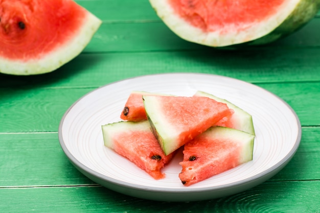 Geschnittene Wassermelone auf einer Platte und ungeschnittene Wassermelone auf einem grünen Holztisch